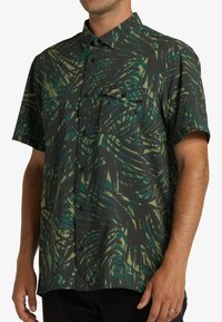 Short-sleeve button-up shirt in dark green with a palm leaf pattern. Features a chest pocket and textured fabric with a relaxed fit.