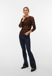 Haut en dentelle florale marron à manches longues et coupe ajustée, associé à un jean évasé bleu foncé et des chaussures marron pointues. Textures de tissu lisses.