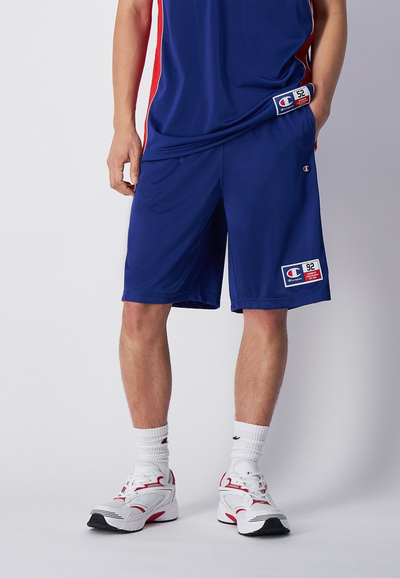 Pantalones cortos deportivos de la Marina con acentos rojos en los laterales, fabricados con una tela ligera. Presenta un parche con el logo y una cinturilla elástica para mayor comodidad.