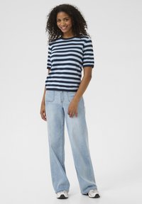 Top a maniche corte a righe navy e azzurro chiaro abbinato a jeans a gamba larga azzurro chiaro e sneaker bianco e nero. Look semplice e comodo.