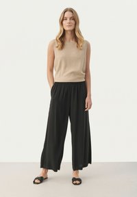 Top sans manches beige associé à un pantalon noir ample et des sandales noires. Le tissu semble doux avec une taille extensible sur le pantalon.