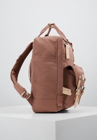 Ruskea kangaskassi, jolla on jämäkkä muoto, sisältäen nahkaosia, säädettävät hihnat ja sivutaskun, jossa on läppä suljettuna.