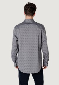 Camisa de manga larga gris con un patrón sutil, hecha de un tejido ligero. Cuenta con un collar y puños abotonados, con un dobladillo curvado.