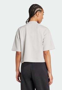 Camiseta gris claro recortada con un tejido texturizado, mangas cortas y un dobladillo recto. Vista desde atrás, llevada con pantalones oscuros.