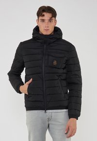 Giacca a vento nera con cappuccio, design a righe orizzontali, chiusura frontale con zip e tasche, e un piccolo logo sul petto.
