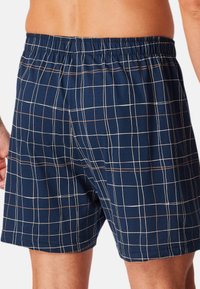 Boxer in blu navy con motivo a griglia in bianco e marrone. Vita elastica, tessuto morbido e design di lunghezza fino a metà coscia.
