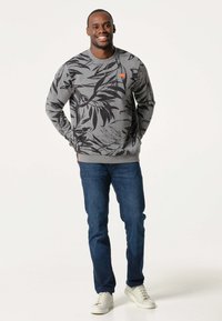 Grijze sweatshirt met zwart bladvormpatroon, ronde hals, geribde boorden en zoom. Gecombineerd met blauwe jeans en witte sneakers.