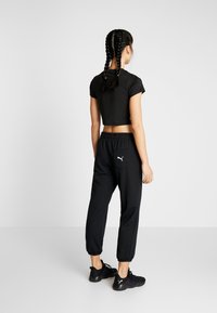 Zwart cropped t-shirt en zwarte joggers met een elastische tailleband. De joggers hebben een achterzak met een wit logo. Het schoeisel bestaat uit zwarte sportschoenen.