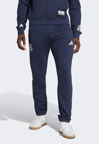 Mornarskoplav sweatshirt Adidas i odgovarajući dukserice. Sweatshirt ima logotip s prednje strane, a dukserice imaju logotip na butini i bočne pruge.