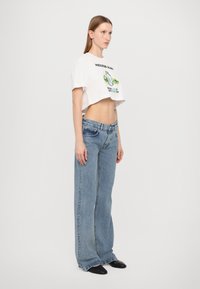 Hvit kortermet t-skjorte med grafisk trykk, kombinert med lys blå vide jeans som har en liten falming og fem lommer. Svarte spisse sko.