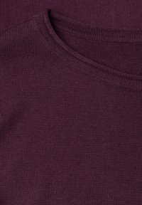 Gros plan d’un pull en maille violet foncé plié montrant l’encolure ronde et la texture fine du tricot.
