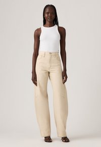 Beige wijdvallende jeans van denim, met een hoge taille, voorzakken met stikdetails en een relaxed fit. Gecombineerd met een witte tanktop.