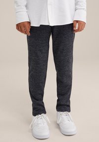 Tamsiai mėlynos tekstūruotos sportinės kelnės su slim fit kirpimu, derinamos su baltais sportbačiais. Marškiniai turi užsegimo mygtukais dizainą ir ilgomis rankovėmis, pagaminti iš lengvos medžiagos.