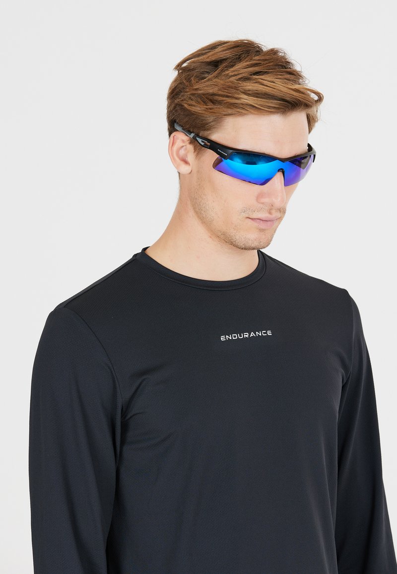 Sports solbriller med en blank sort ramme, blå spejlglas og et strømlinet design. Båret med en sort langærmet sports T-shirt.