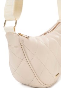 Borsa a tracolla in crema trapuntata con forma curva, texture liscia, zip dorata e tracolla regolabile in tessuto. Presenta dettagli di cucitura a contrasto.