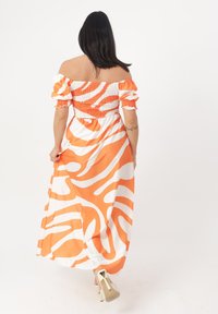 Maxikleid in orange und weißem Wellenmuster, schulterfreies Design, strukturierter Smock-Oberteil, fließender Stoff, mit sichtbarem Schmuck.