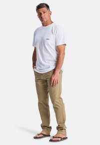 Hvid bomulds T-shirt med brystlomme, tan twill bukser og sorte flip-flops. Enkelt design, afslappet pasform og let tekstur.