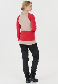 Tight, långärmad topp i röd och beige med en texturerad design; ihopparad med svarta, hållbara byxor och vandringskängor.