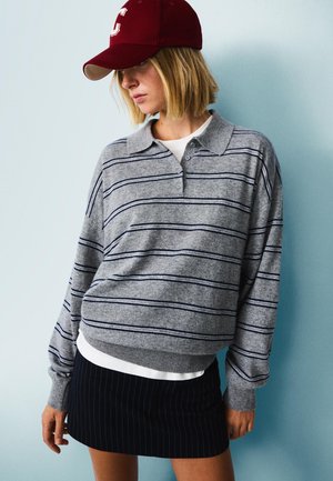 Gray striped sweater with a collared neckline, paired with a white top and a navy pinstripe skirt, complemented by a maroon cap.