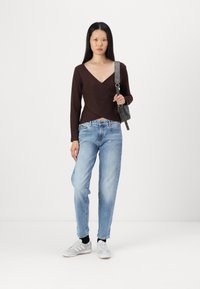 Pull enroulé marron, jean bleu clair, baskets gris et blanc avec des chaussettes noires. Sac minimaliste noir avec bandoulière.