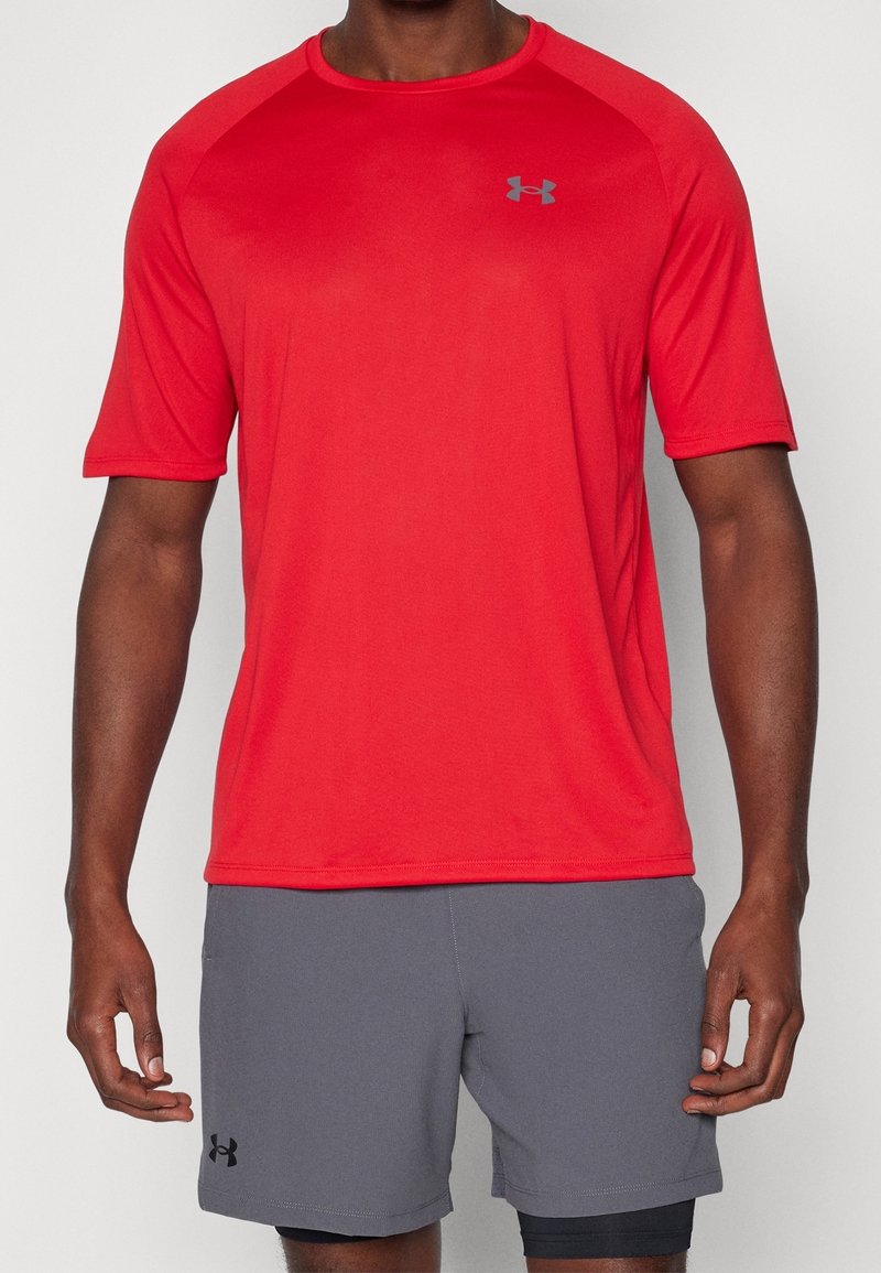 Camiseta atlética roja de manga corta con cuello redondo y logo gris. Llevada con pantalones cortos grises. Textura suave, tela transpirable.