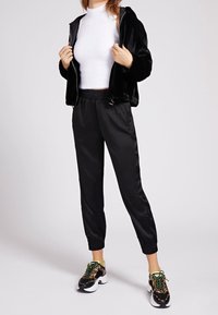 Black faux fur zip-up hoodie, white fitted turtleneck, black satin joggers, and patterned sneakers with green accents.