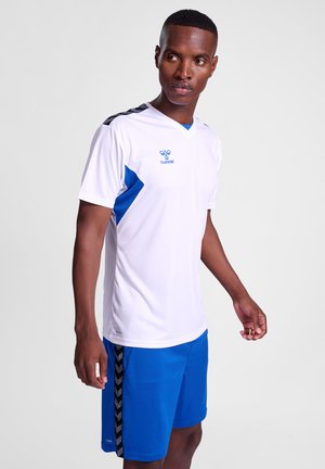 Hvid atletisk trøje med blå detaljer, featuring en v-hals og sorte skulderstriber. Parret med blå shorts, der viser et sort chevronmønster.