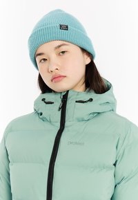 Lichtblauwe gebreide beanie en mintgroene ritssluiting puffervest met een zwarte ritssluiting en logo, voorzien van een capuchon en gestikte panelontwerp.