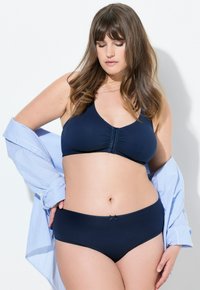 Reggiseno e culotte blu navy realizzati in tessuto morbido, con chiusura frontale e un piccolo dettaglio a fiocco sulle mutande, abbinati a una camicia a righe chiare.
