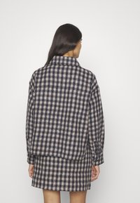 Veste surdimensionnée en mélange de laine avec un motif à carreaux bleu marine et beige. Présente une texture douce, un large col et des fentes latérales pour faciliter le mouvement.