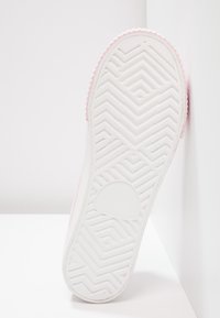 Podeszwa buta z białą, teksturowaną gumową podstawą ozdobioną wzorem w jodełkę. Górna krawędź ma delikatną, różową lamówkę wzdłuż boku.