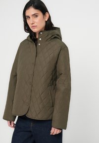 Πράσινο χακί μπουφάν με κουκούλα, με κούμπωμα με κουμπιά και πλαϊνές τσέπες. Το ύφασμα έχει λεία, ελαφρώς γυαλιστερή υφή.