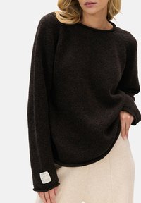 Brązowy sweter dziany o swobodnym kroju, z okrągłym dekoltem i prążkowanymi mankietami. Posiada wszywaną metkę na rękawie oraz teksturowany wzór.