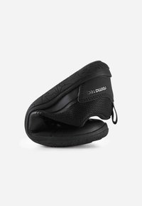 Chaussure noire flexible pliée en deux, avec semelle texturée, empeigne en tissu maille et languette avec étiquette "reima TEC".