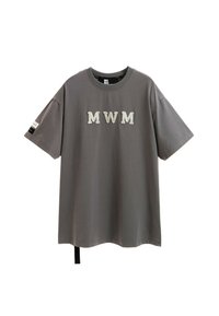 Camiseta gris de gran tamaño con "MWM" bordado en la parte frontal, mangas cortas y tela texturizada. Presenta una etiqueta negra en la manga izquierda.