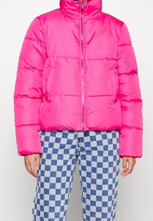 Hellrosa gestepptes Jacke mit Reißverschluss, getragen zu blau-weiß karierten Hosen, Hände seitlich liegend, vor einfachem Hintergrund.