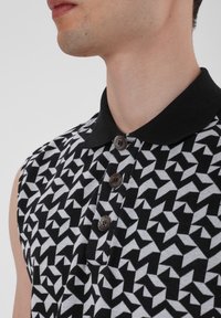Sleeveless black and white polo shirt featuring a geometric pattern, a black collar, and brown plastic buttons on the placket.