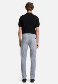 Polo shirt noir à manches courtes associé à un jean gris clair. Le jean possède deux poches arrière et une coupe classique. Des chaussures noires complètent la tenue.