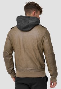 Brun læderjakke med en grå stofhætte, ribbede manchetter og et tætsiddende design. Bemærkelsesværdige skulderepauletter og quiltet accent syning.