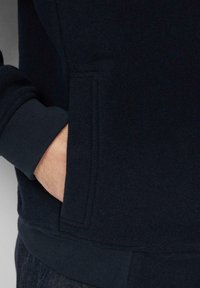 Granatowy sweatshirt z miękkiego materiału, z boczną kieszenią oraz ściągaczami na mankietach i dolnym wykończeniu. Gładka faktura z minimalnymi detalami szwów.