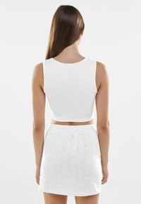 Vit cropped linne i ribbad bomull som är kombinerat med en vit broderad minikjol med öggelmönster och resårmidja.