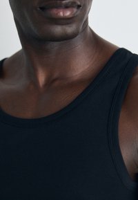 Sort bomulds tanktop med rund halsudskæring og brede stropper, der har en glat tekstur og minimal syning.