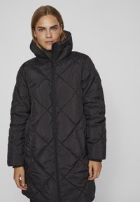 Črn podloženi dolgi plašč z visokim ovratnikom, ki ima sprednji zadrgo in stranske žepe, izdelan iz lahkega materiala z gladko teksturo.