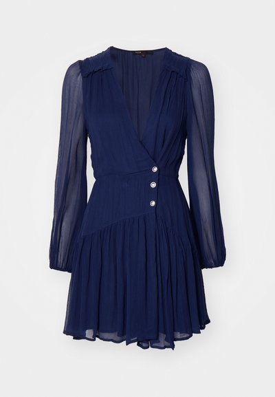 Marineblauwe jurk met lange, doorzichtige mouwen, diepe v-hals en gathered rok. Heeft decoratieve knopen op de taille en een gestructureerde stof.