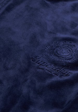 Granatowa tkanina polarowa o miękkiej fakturze z wytłoczonym logo Superdry i misternymi zdobieniami.