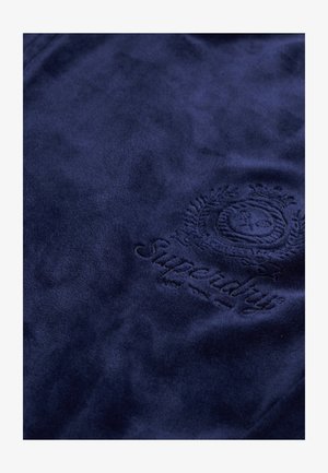 Granatowa tkanina polarowa o miękkiej fakturze z wytłoczonym logo Superdry i misternymi zdobieniami.