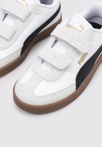 Sneakers bianchi e neri con cinturini in velcro, caratterizzati da una tomaia in suede e sintetico, suola in gomma e accenti di branding dorati.