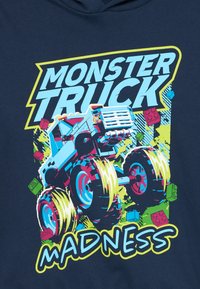 Il sudore navy presenta un grafico con un camion mostro blu dotato di ruote sovradimensionate, blocchi Lego colorati e il testo audace "MONSTER TRUCK MADNESS".