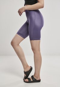 Lila högmidjade cykelshorts i slät, stretchig tyg, matchade med svarta sandaler med öppen tå och spännen.
