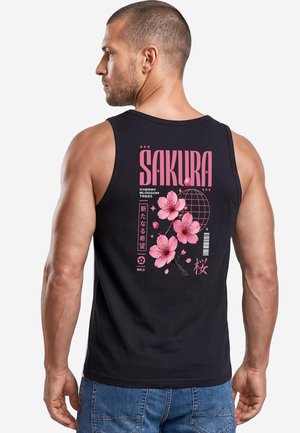 Mann mit kurzen Haaren, der ein schwarzes ärmelloses Shirt mit pinker Kirschblütengrafik und dem Text "SAKURA" auf dem Rücken trägt.